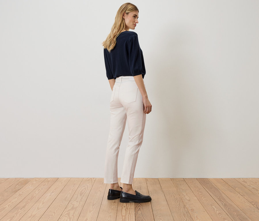 Kobieta stoi tyłem, ma na sobie granatową bluzkę, różowe dżinsy i czarne buty.