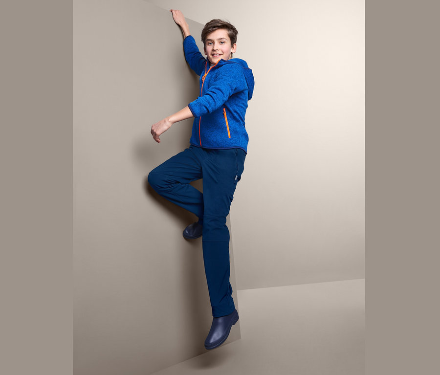 Chłopiec wspina się po rogu ściany, ubrany w niebieskie spodnie softshell.