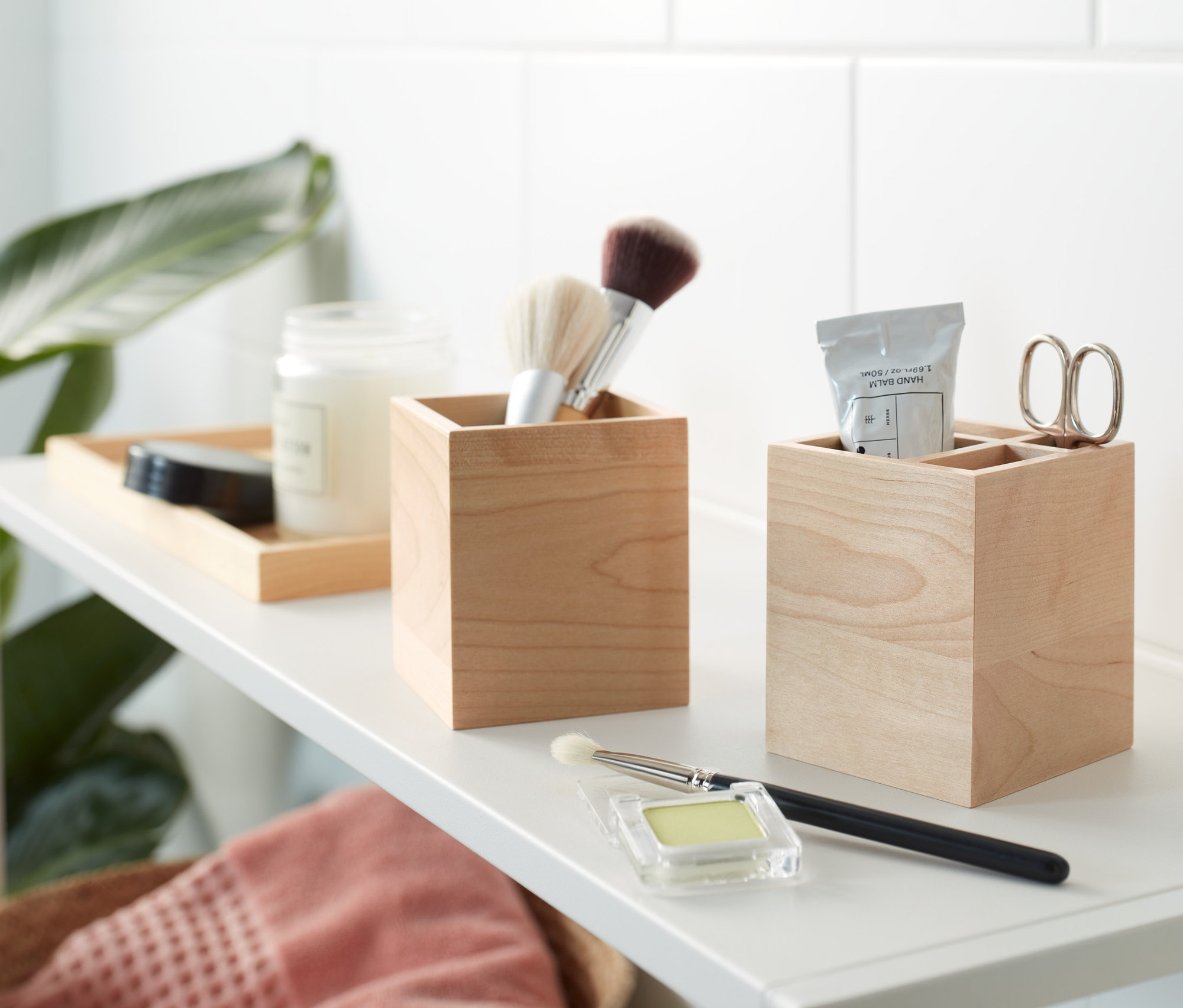 Dwa drewniane pudełka do przechowywania na białej półce, jedno z pędzlami do makijażu, drugie z nożyczkami i kremem.
