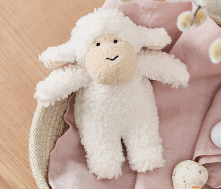 Owieczka z dźwiękiem leży w koszyku z gałązkami wierzby i malowanymi jajkami.