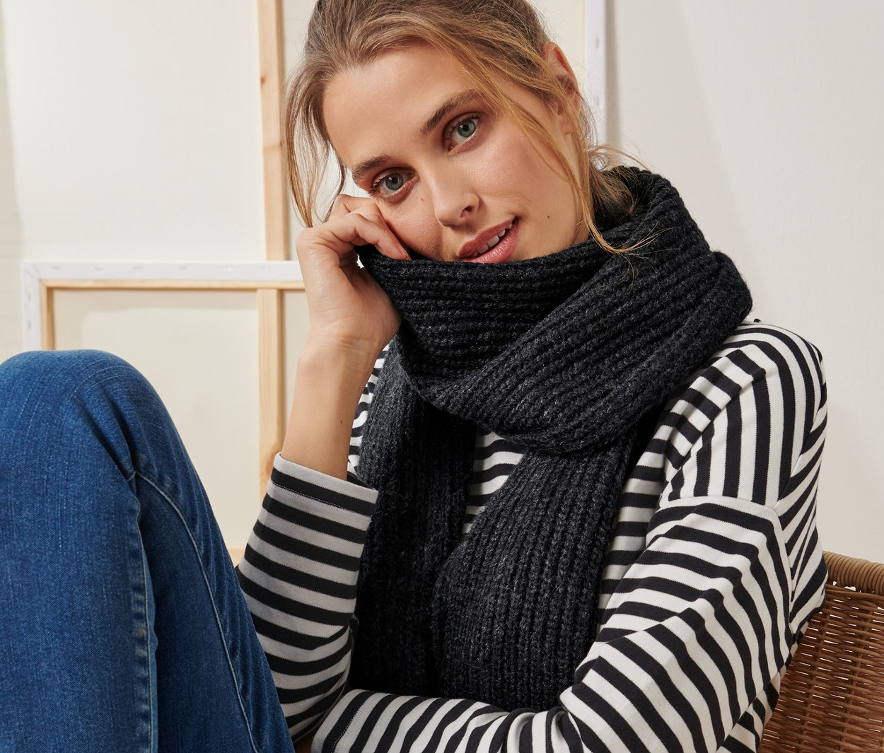 Kobieta siedzi na krześle i ma na sobie antracytowy szalik z dzianiny.