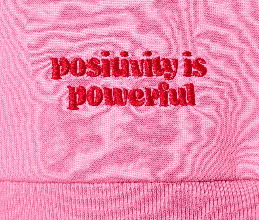 Zbliżenie na różową bluzę dresową z czerwonym haftem "positivity is powerful".