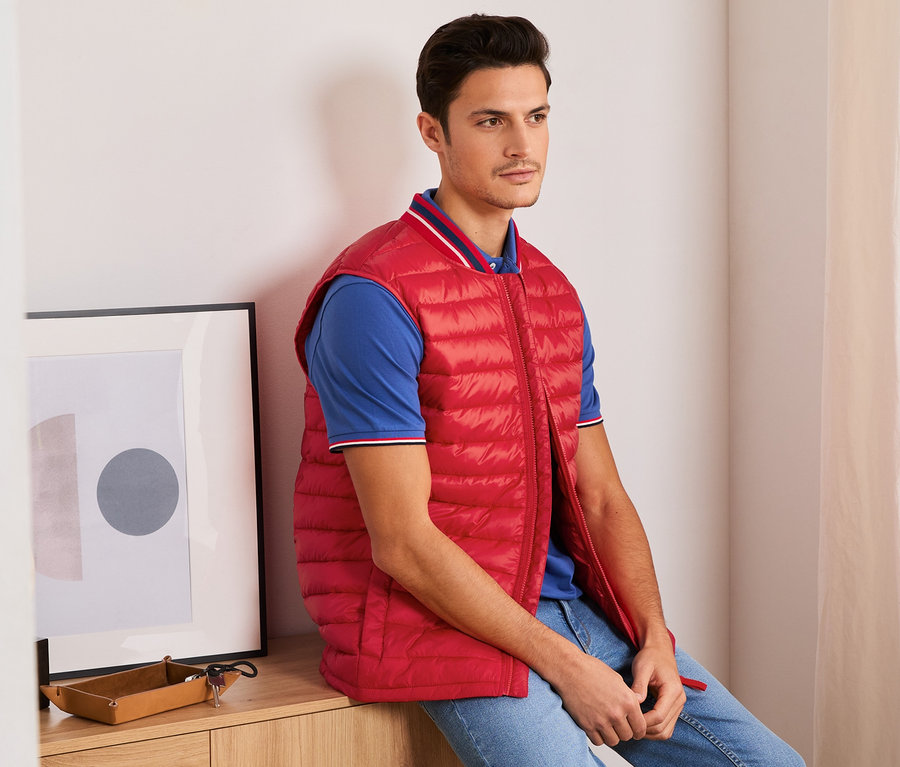 Mężczyzna siedzi w czerwonej kamizelce pikowanej.