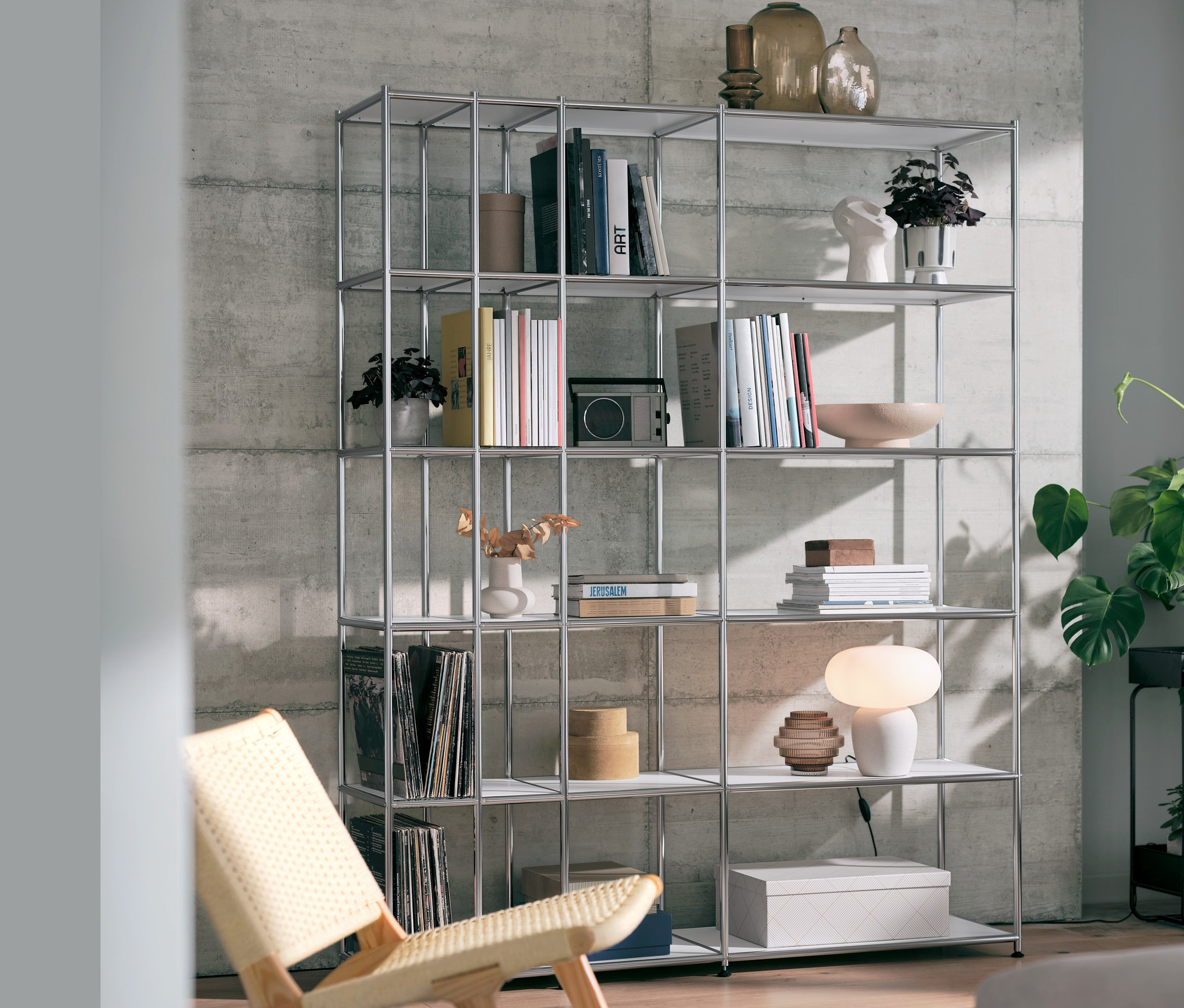 Otwarty regał metalowy »CN3« biały z lampką stołową ze szklanym abażurem i fotelem.