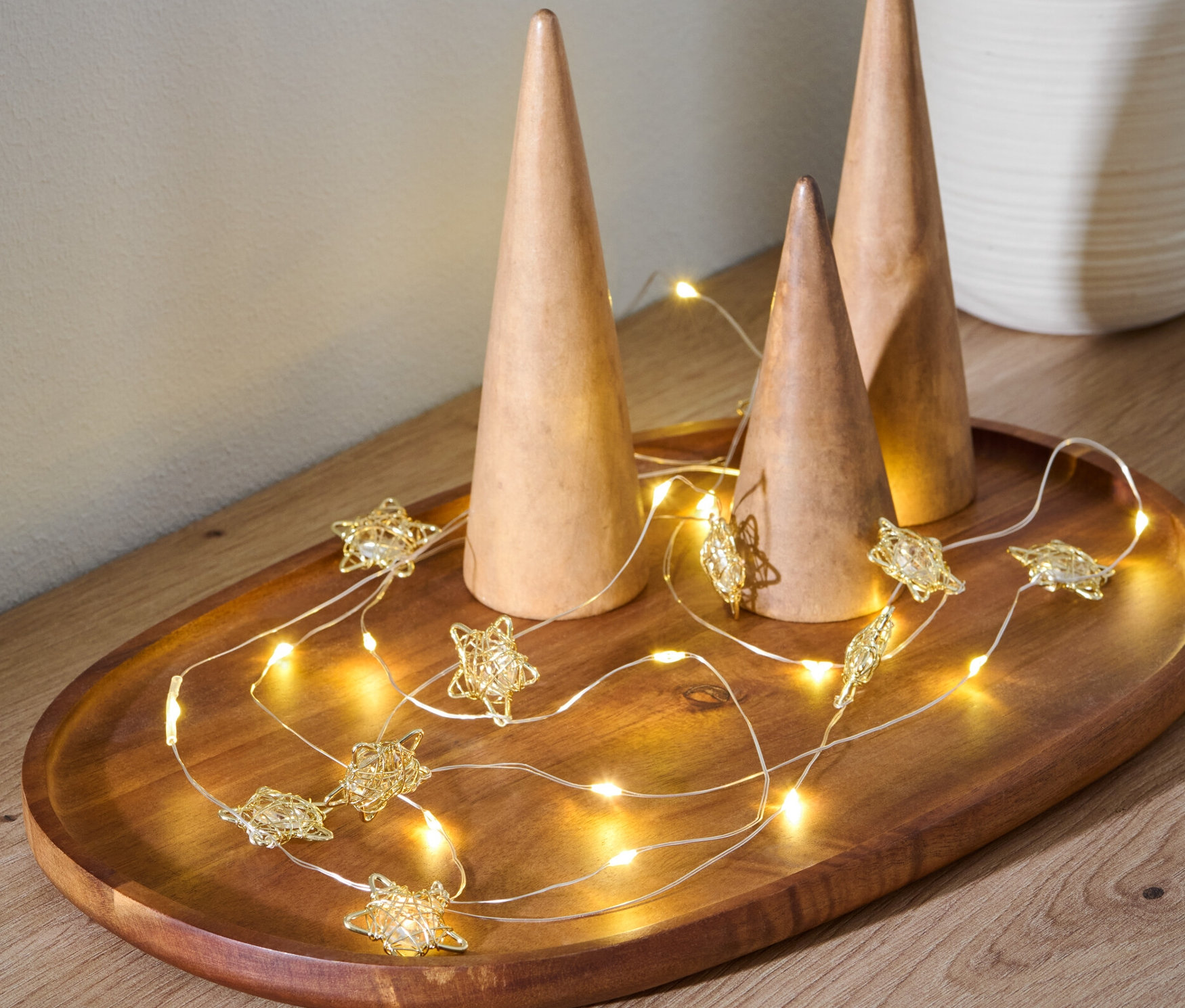 Na drewnianej tacy leżą trzy drewniane stożki i łańcuch świetlny LED w kształcie gwiazdy.
