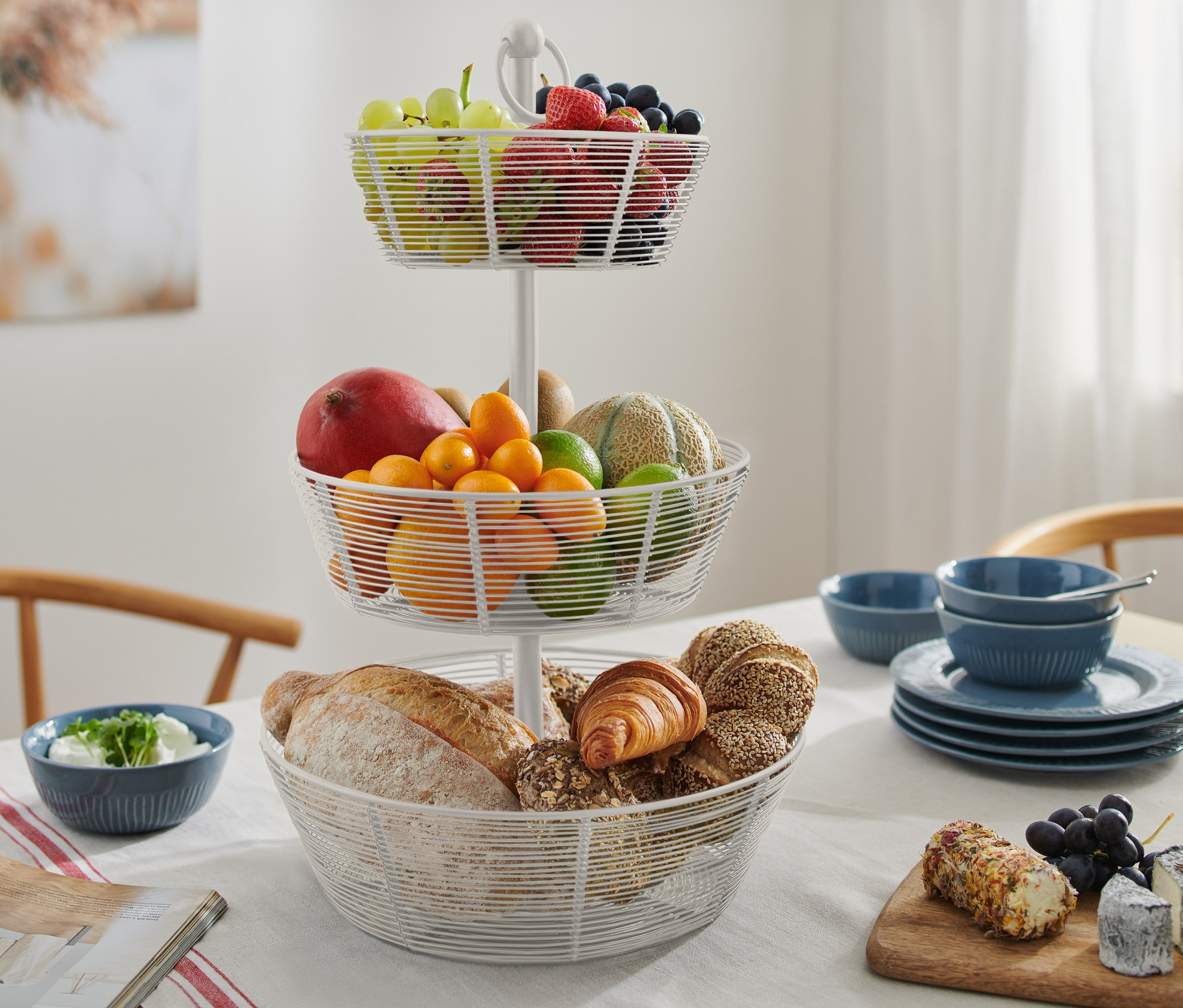 Trzypoziomowa etażerka z owocami i pieczywem na stole.