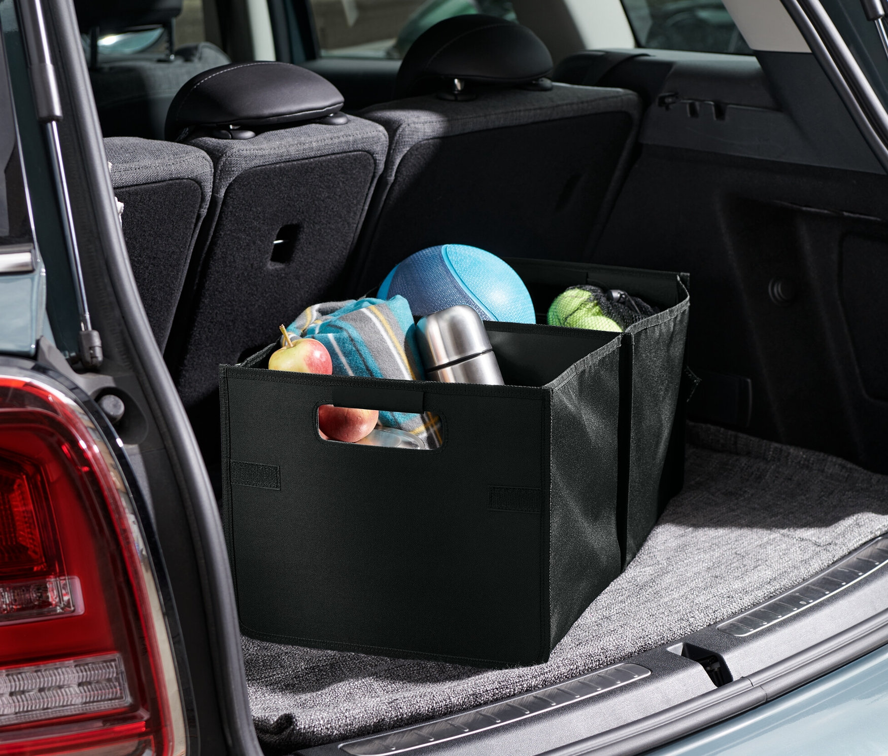 Składany organizer do samochodu znajduje się w bagażniku samochodu, wewnątrz pudełka znajdują się owoce, koc, termos i piłki.