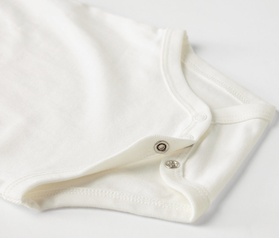 Zbliżenie na białe body niemowlęce z krótkim rękawem i zatrzaskami.