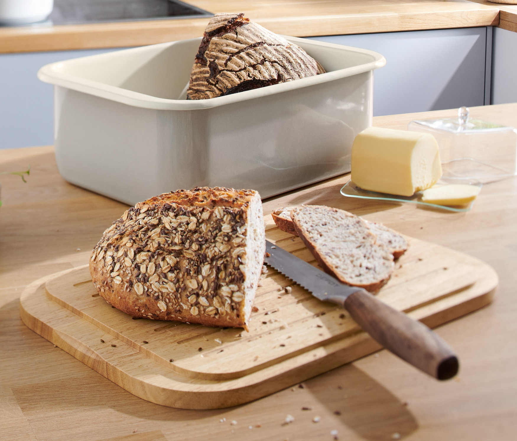 Chleb i pokrojone kromki chleba na desce do krojenia obok emaliowanego chlebaka.