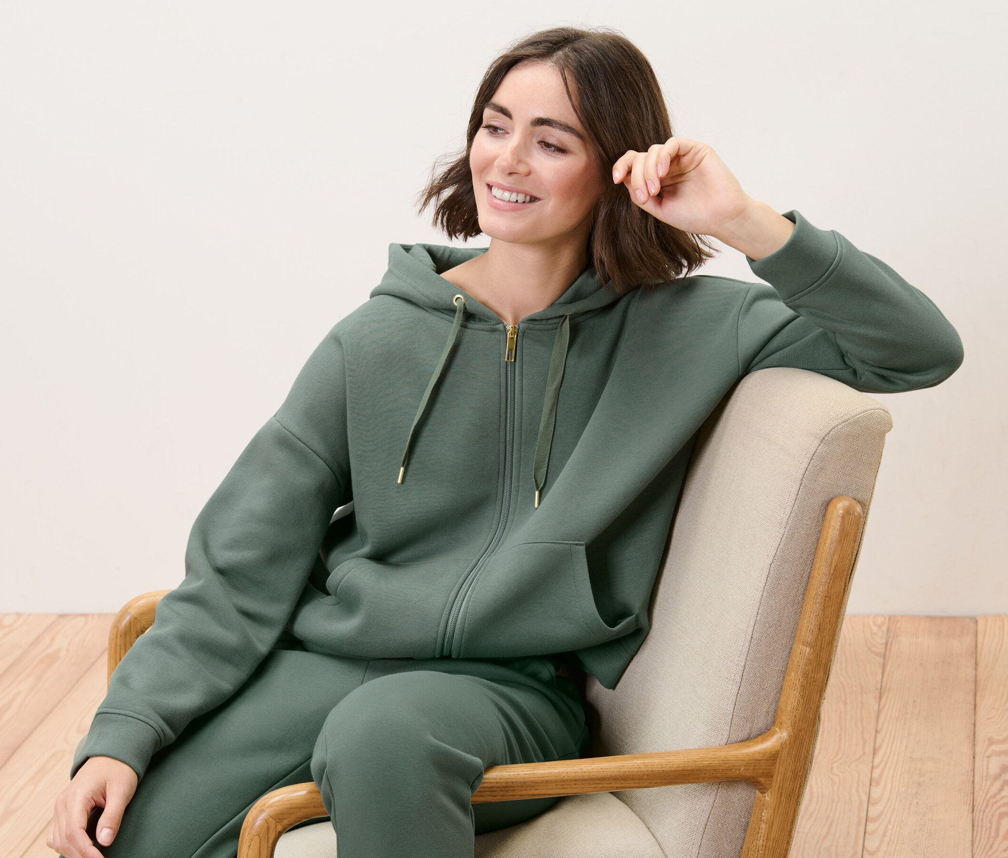 Kobieta siedzi w fotelu i ma na sobie rozpinaną bluzę dresową.