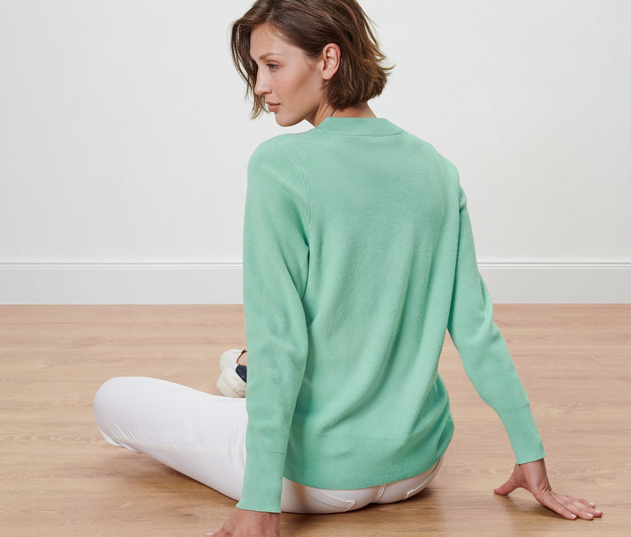 Kobieta siedzi na podłodze w swetrze z dzianiny.