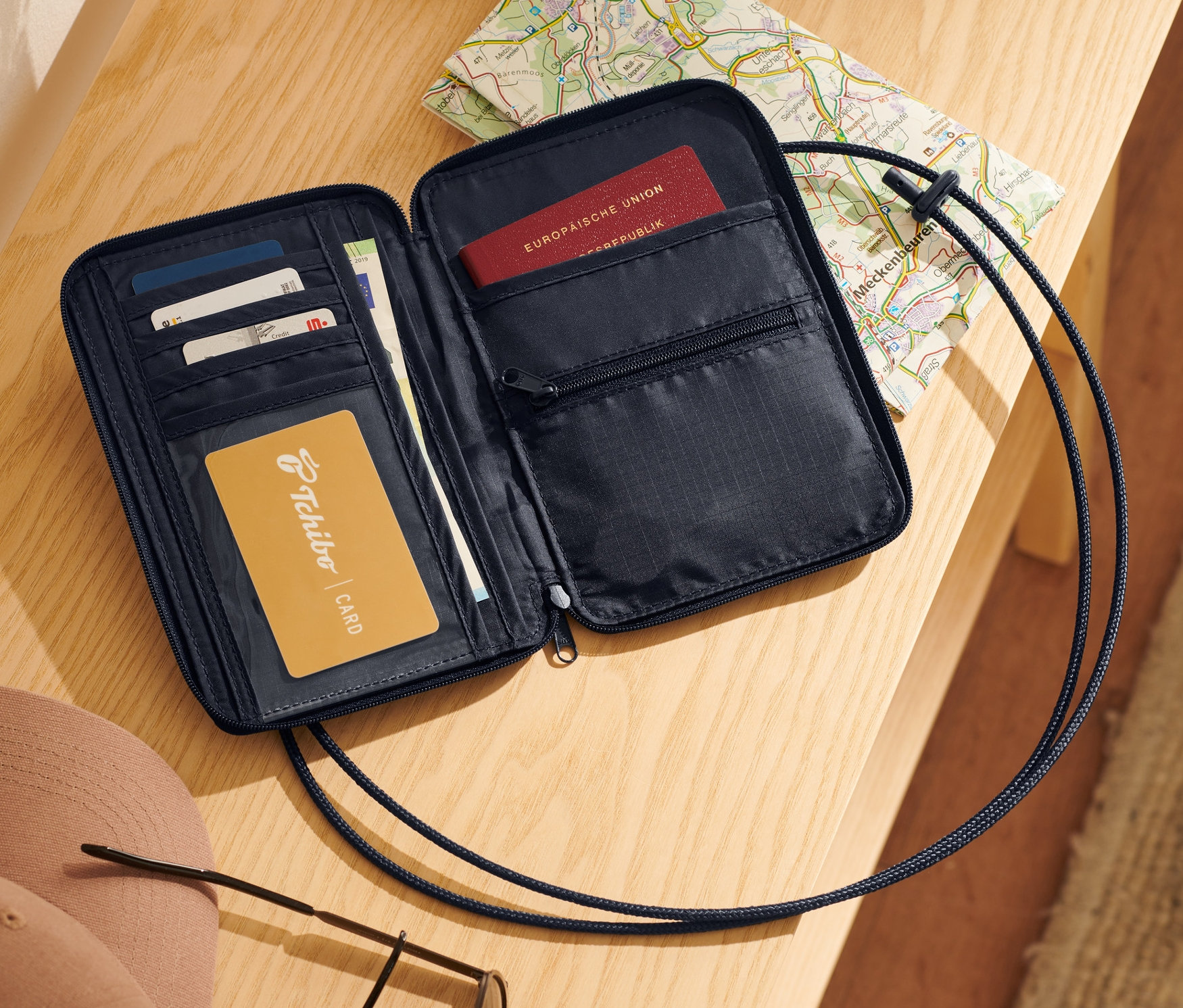 Otwarta czarna torebka na szyję z kartami, paszportem i mapą na drewnianym stole.
