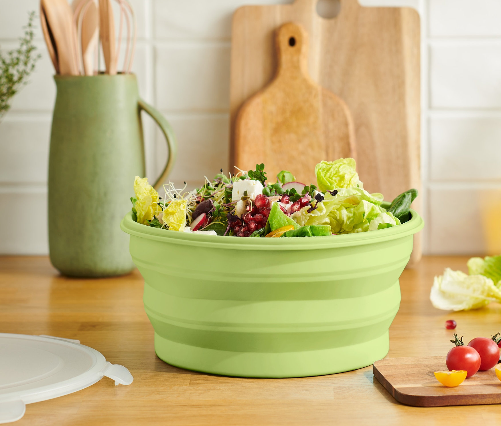 Zielona składana miska na sałatkę wypełniona sałatą na drewnianej desce.