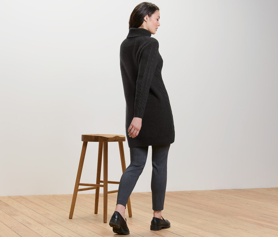 Kobieta odwrócona tyłem ma na sobie długi czarny sweter z warkoczowym wzorem.