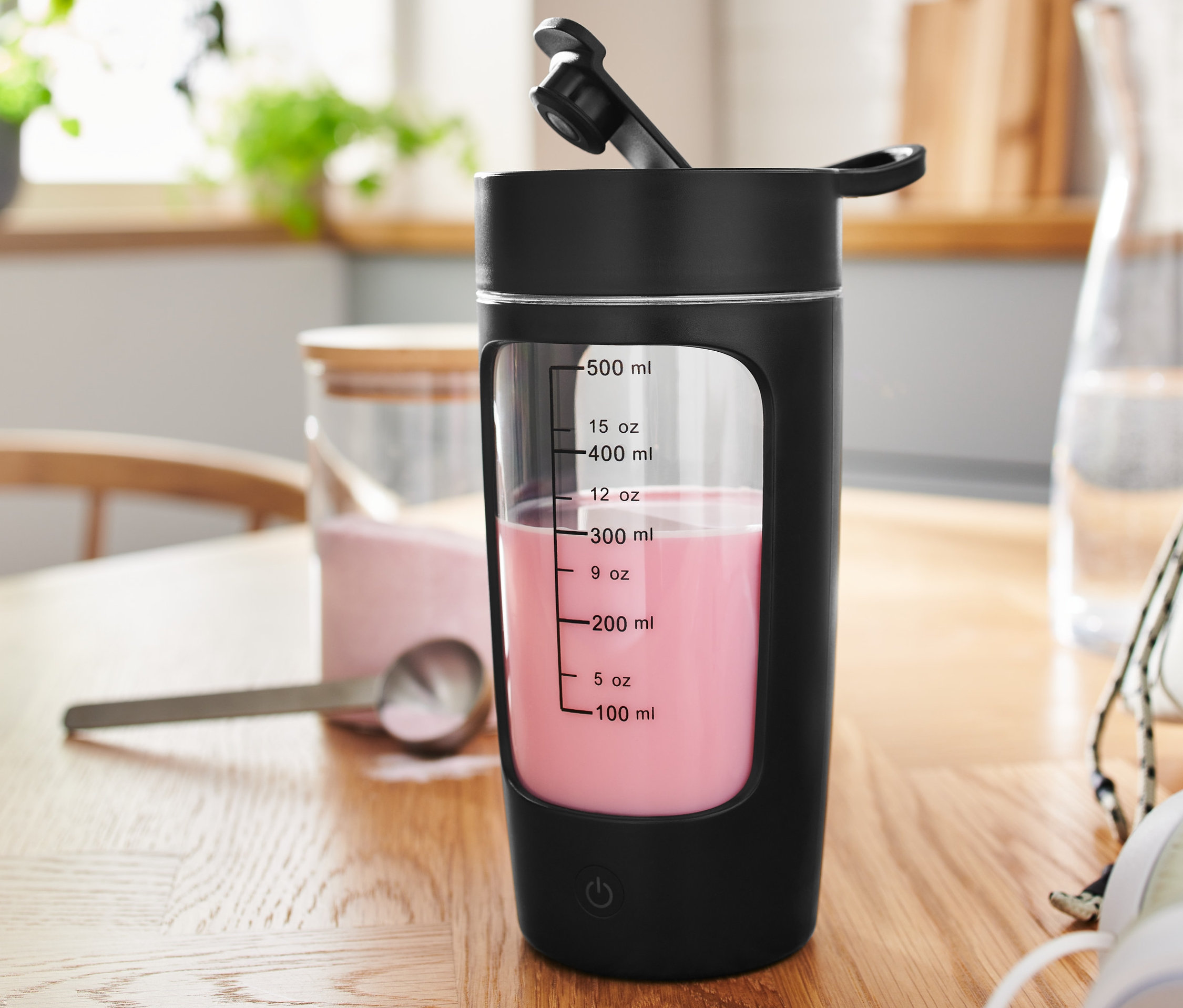 Czarny shaker zasilany akumulatorowo z różowym napojem na drewnianym stole.