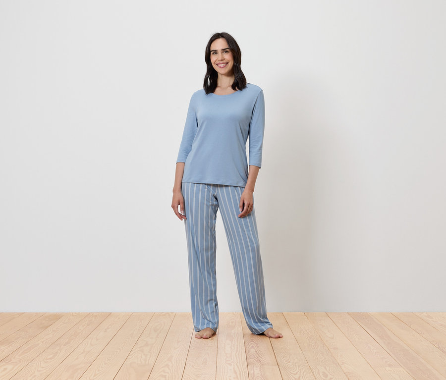 Kobieta stoi w niebieskiej, prążkowanej piżamie.