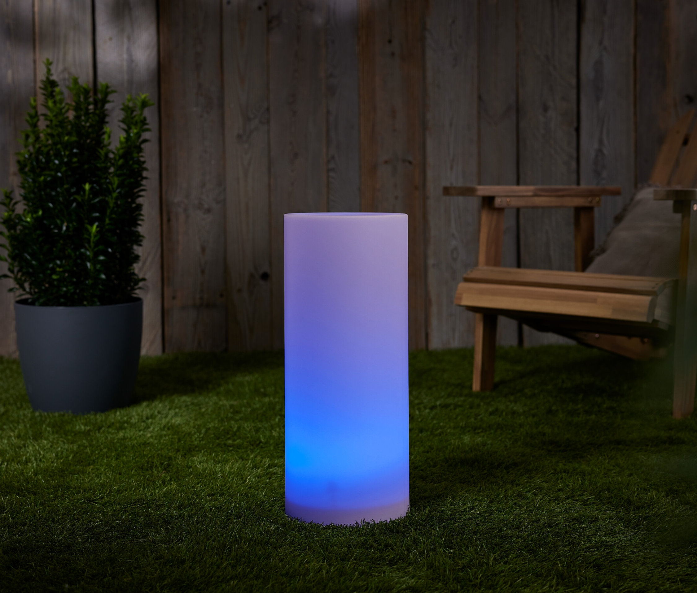 Solarny słupek świetlny z przepływem kolorów, ok. 50 cm, stoi na trawie obok doniczki i drewnianego krzesła.