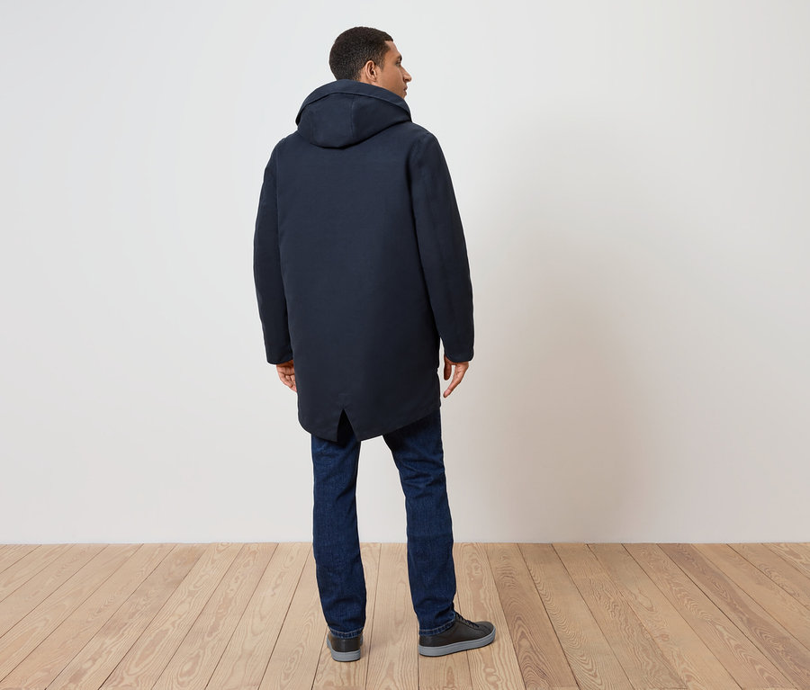Mężczyzna tyłem, ubrany w granatowy płaszcz z kapturem, dżinsy i buty.