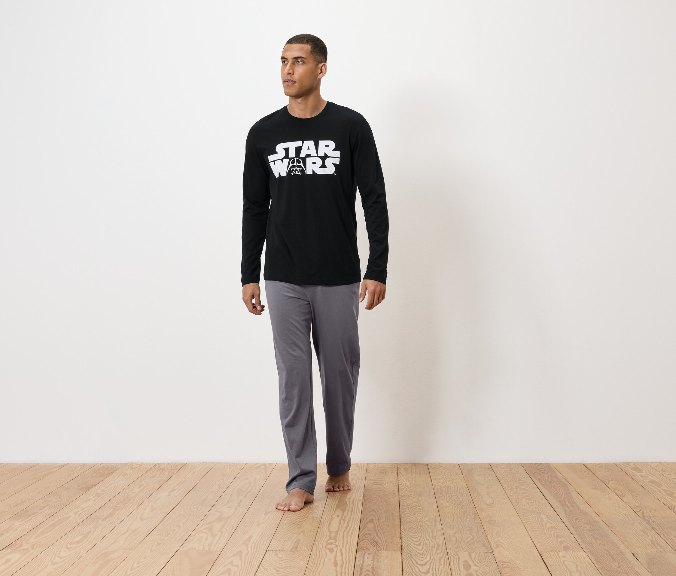 Mężczyzna stoi boso na drewnianej podłodze, ubrany w czarną piżamę Star Wars.