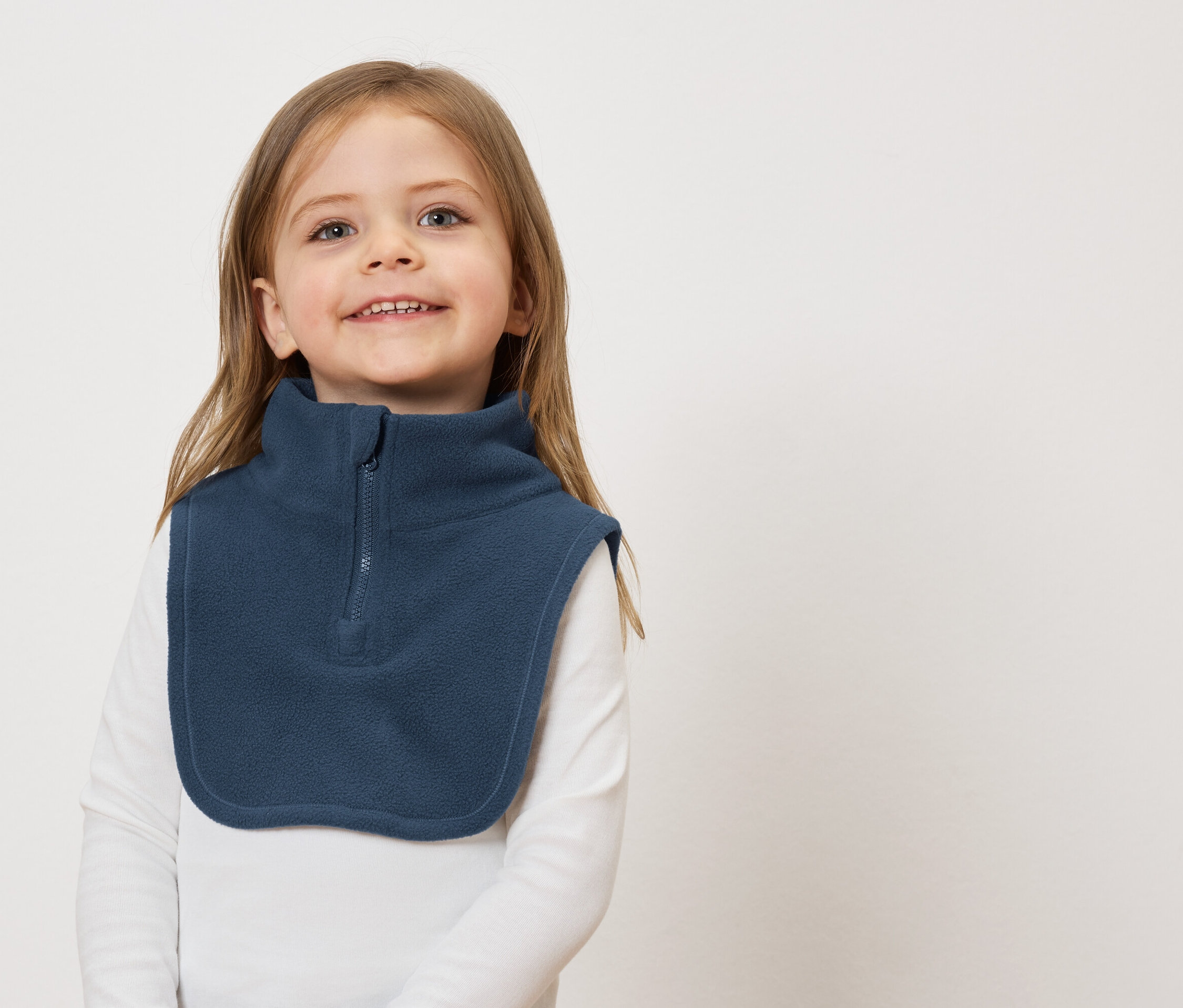 Uśmiechnięta dziewczynka z brązowymi włosami w niebieskim polarowym ocieplaczu na szyję na białym tle.