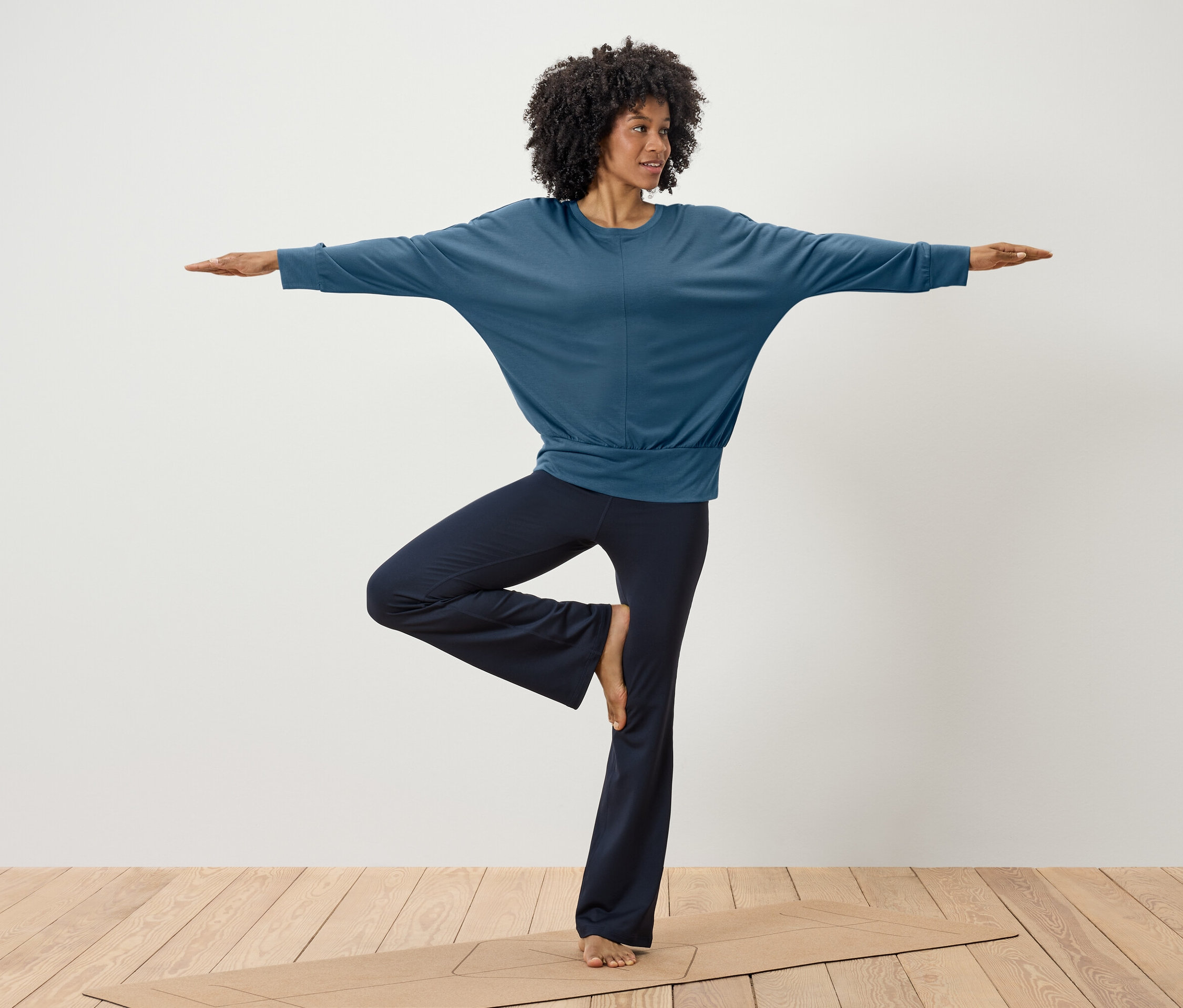 Kobieta ćwiczy jogę w niebieskim topie i granatowych spodniach na macie.