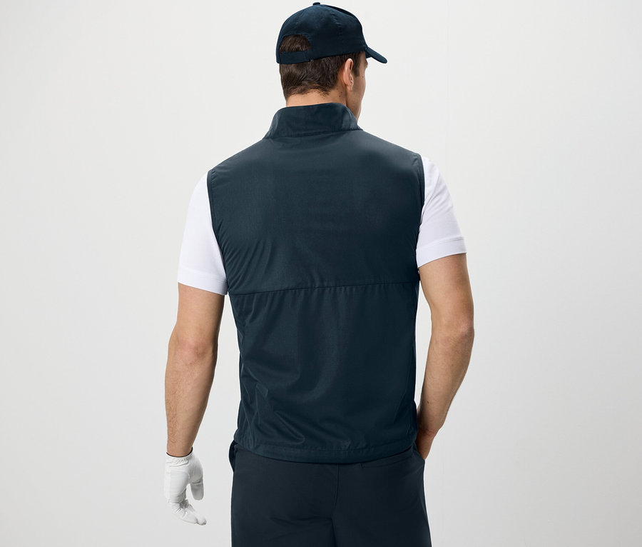 Mężczyzna tyłem do kamery w kamizelce softshellowej, koszulce i czapce z daszkiem.