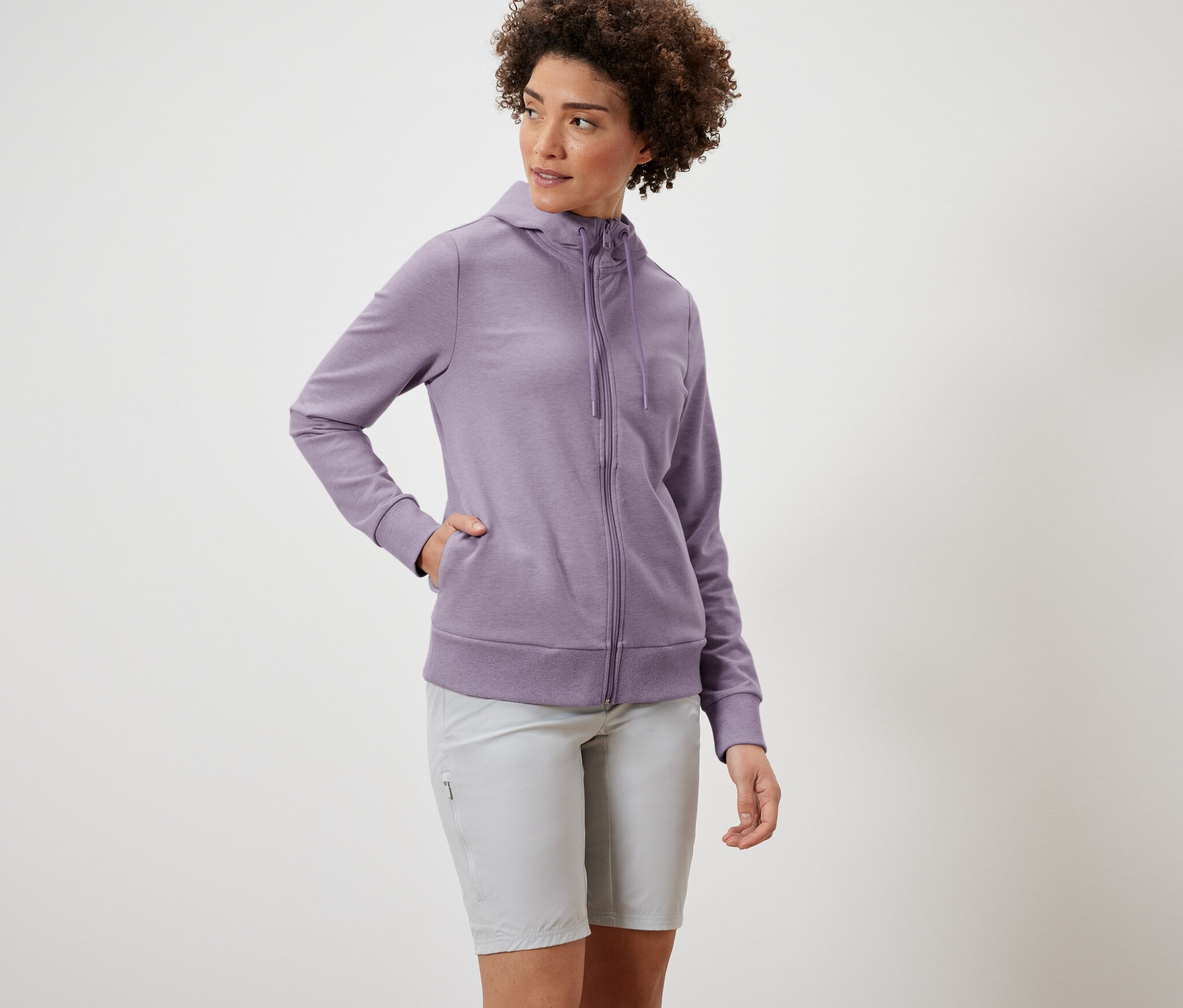 Kobieta ma na sobie fioletową rozpinaną bluzę dresową i szare szorty.
