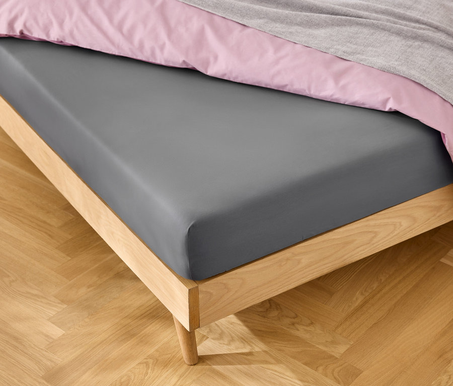 Łóżko z szarym prześcieradłem, różową pościelą i szarym kocem.