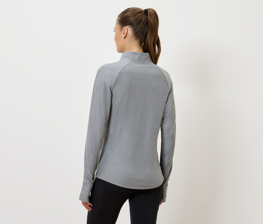 Kobieta tyłem do kamery ma na sobie szarą bluzkę z długim rękawem i czarne spodnie.