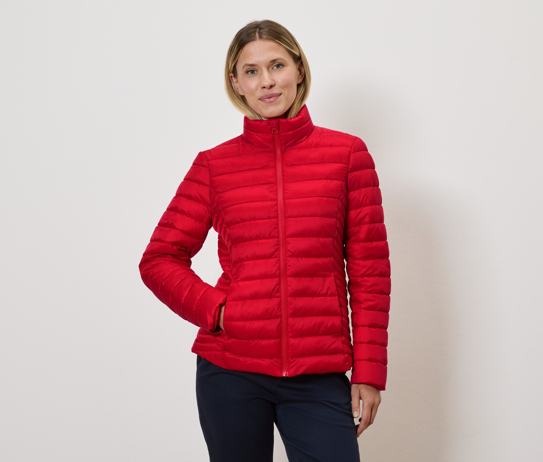 Kobieta pozuje w czerwonej kurtce puchowej.