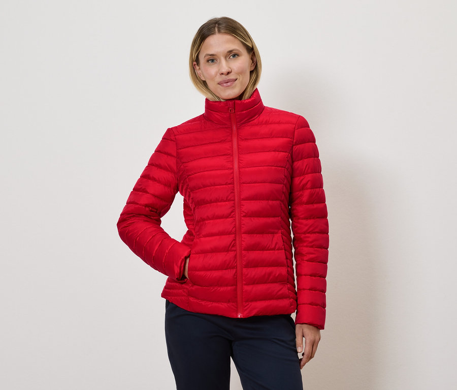 Kobieta pozuje w czerwonej kurtce puchowej.