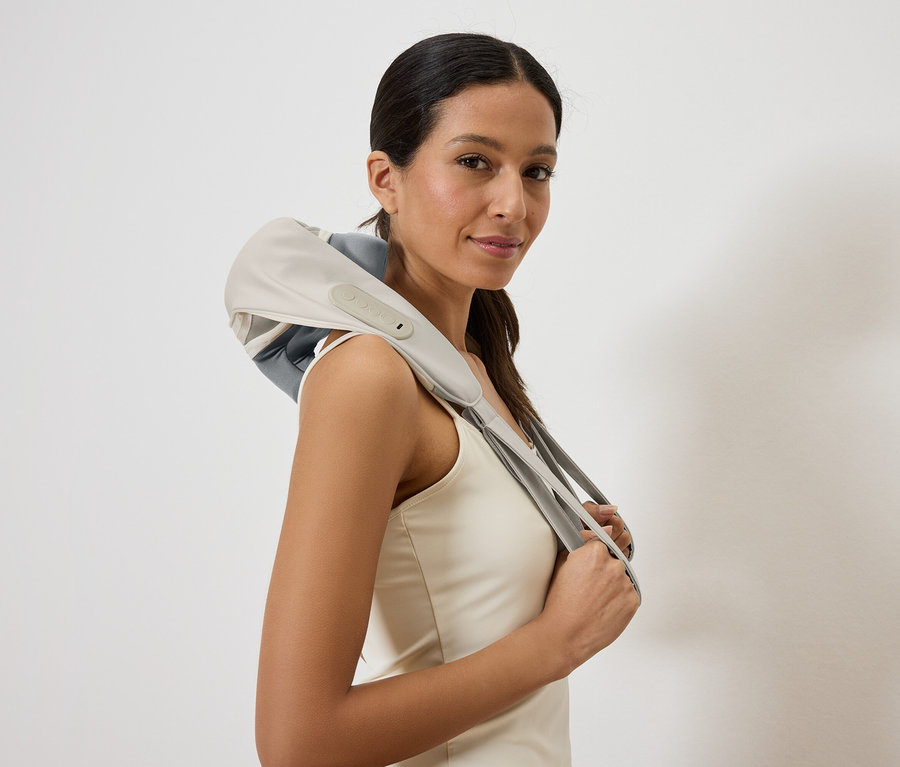 Kobieta z szarym i beżowym masażerem karku na ramionach, trzyma urządzenie rękami.