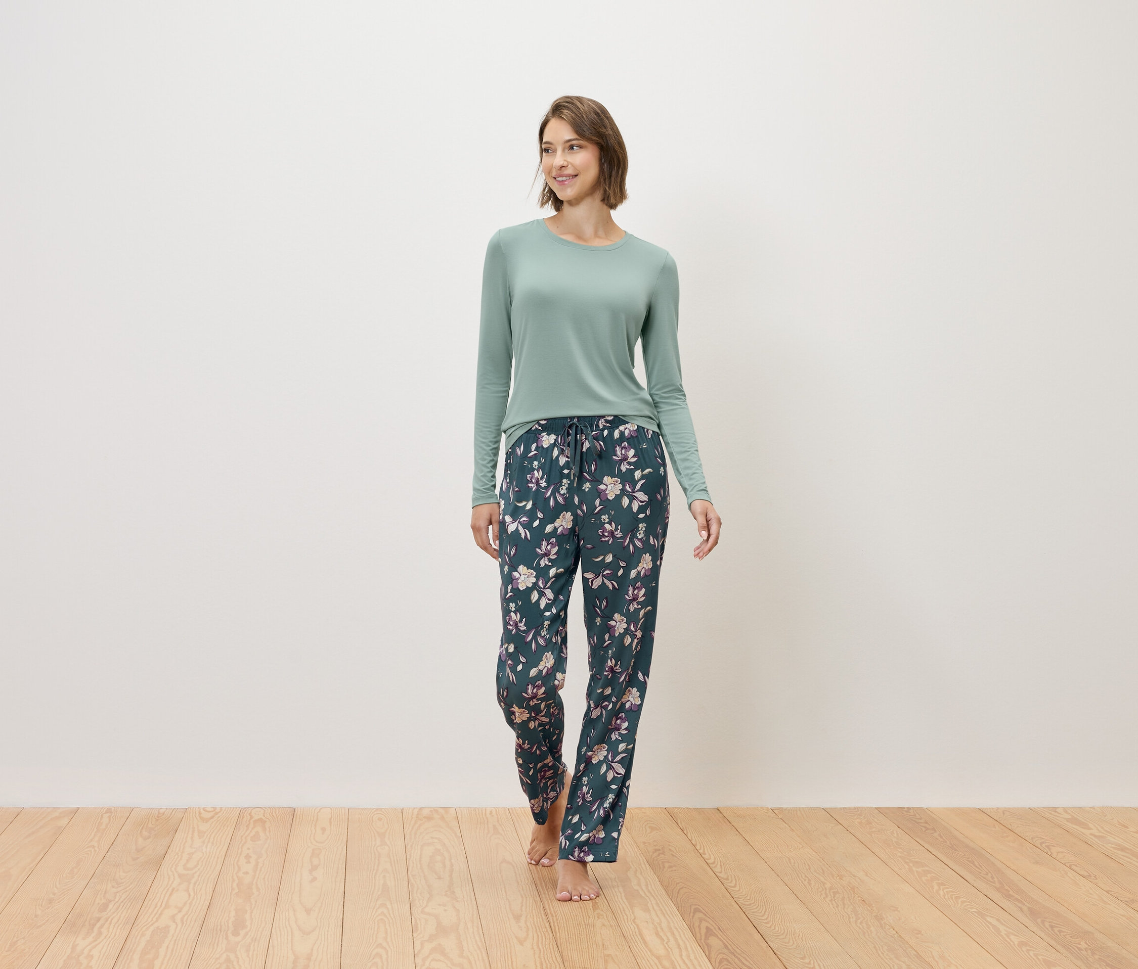 Kobieta idzie boso, ubrana w miętowy sweter i granatowe spodnie od piżamy w kwiatowy wzór.