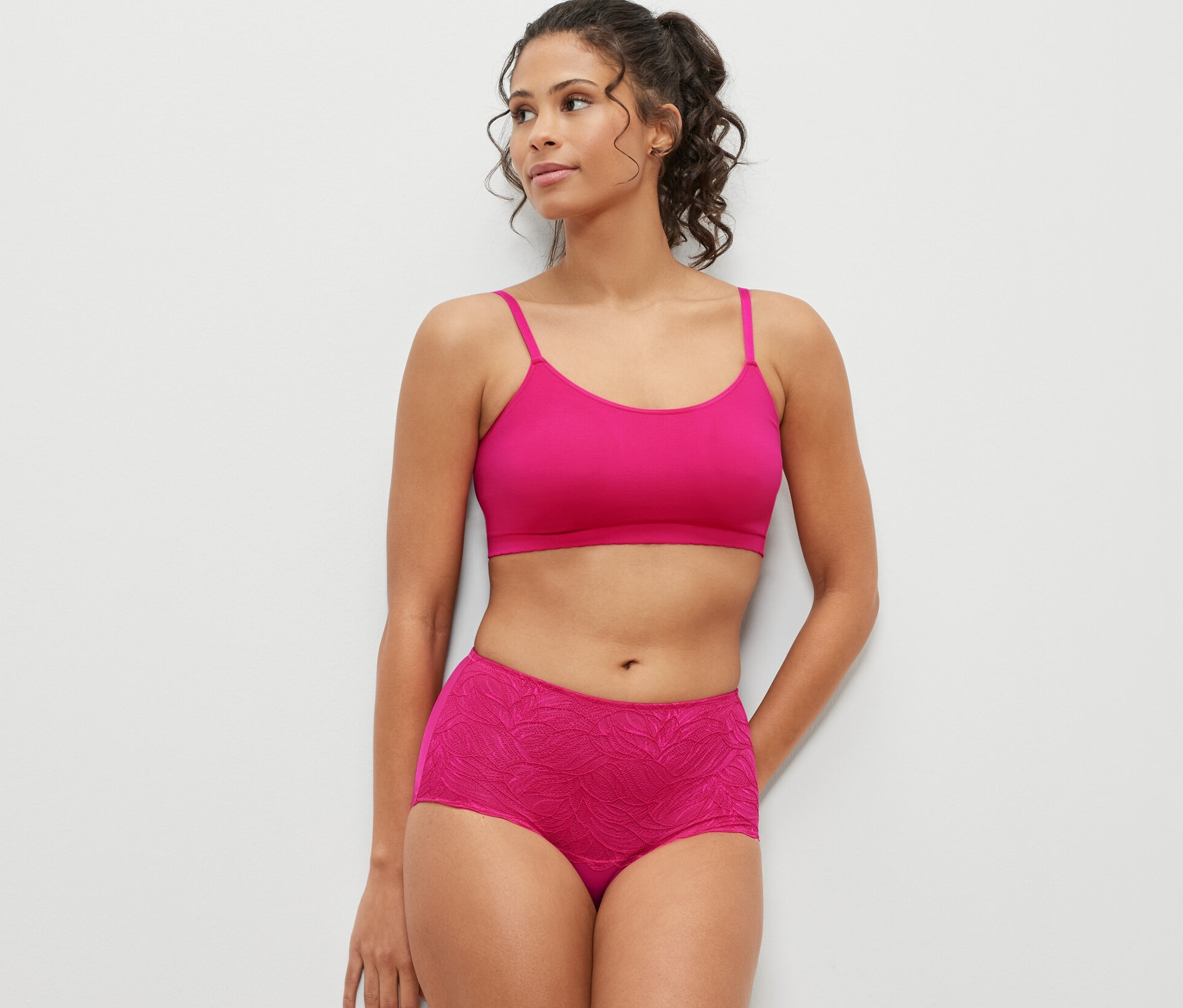 Kobieta pozuje w różowym biustonoszu i lekko modelujących figach z wysokim stanem, fuksja.
