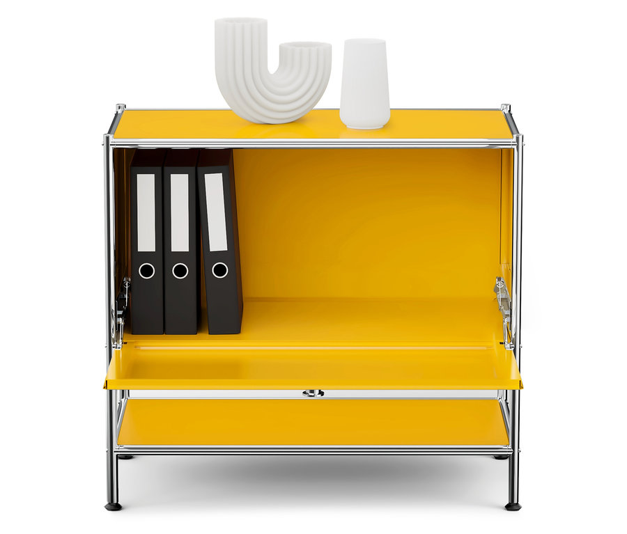 Żółta szafka z chromowaną ramą, wewnątrz trzy czarne segregatory i na górze dwie białe dekoracje.