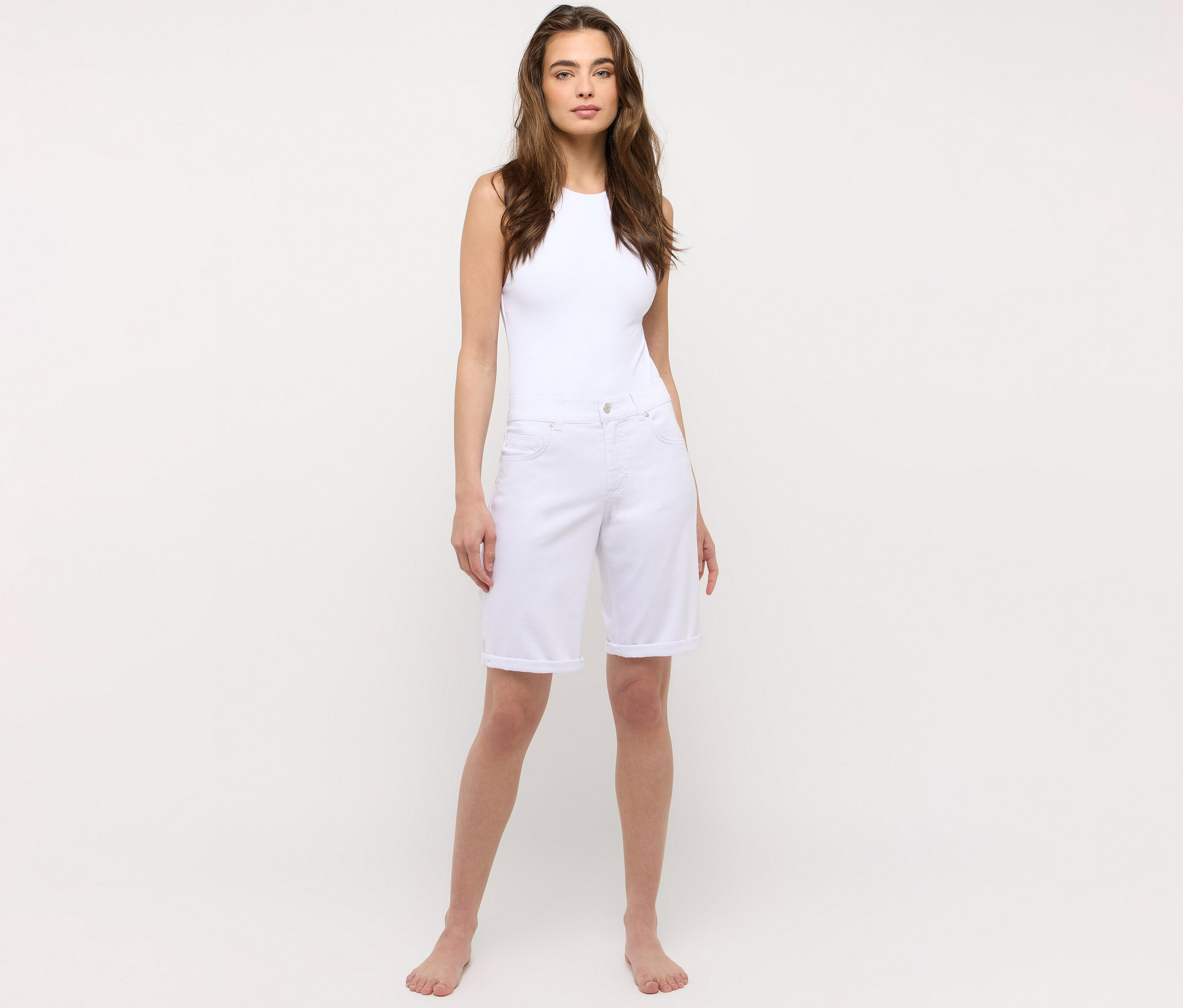 Kobieta stoi boso i ma na sobie biały tank top oraz białe dżinsy Angels „Bermuda Turn-Up” o kroju Straight Fit.