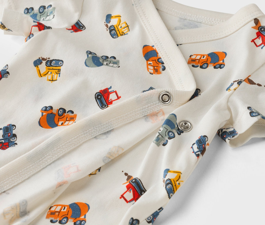 Zbliżenie na białe body dziecięce we wzór z samochodami budowlanymi.