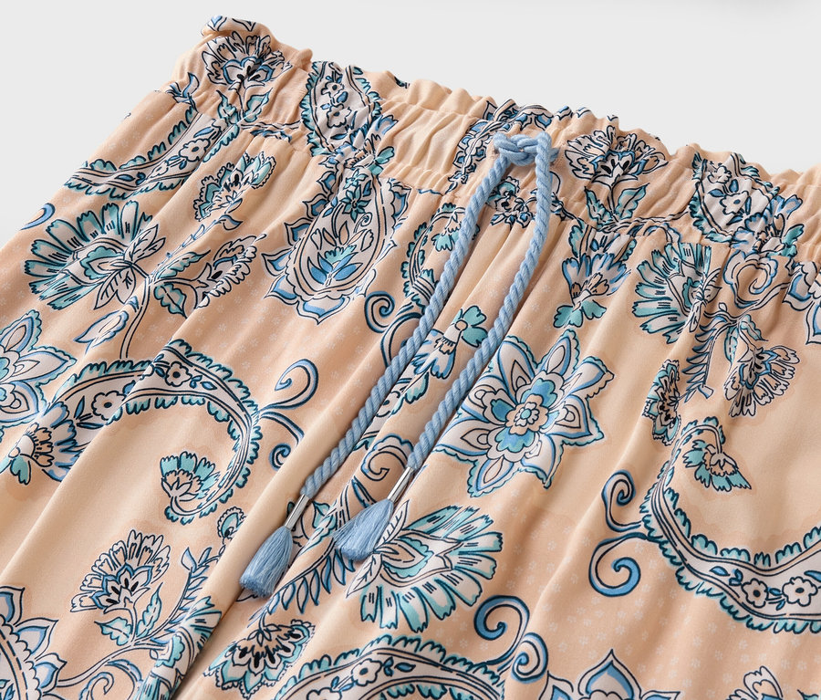 Szczegółowe ujęcie brzoskwiniowych spodni z niebieskim kwiatowym wzorem i sznurkiem.