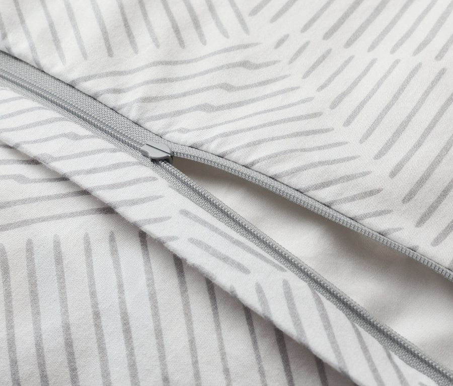 Zbliżenie częściowo otwartej poszwy na kołdrę z zamkiem błyskawicznym i szarym wzorem w paski na białym tle.