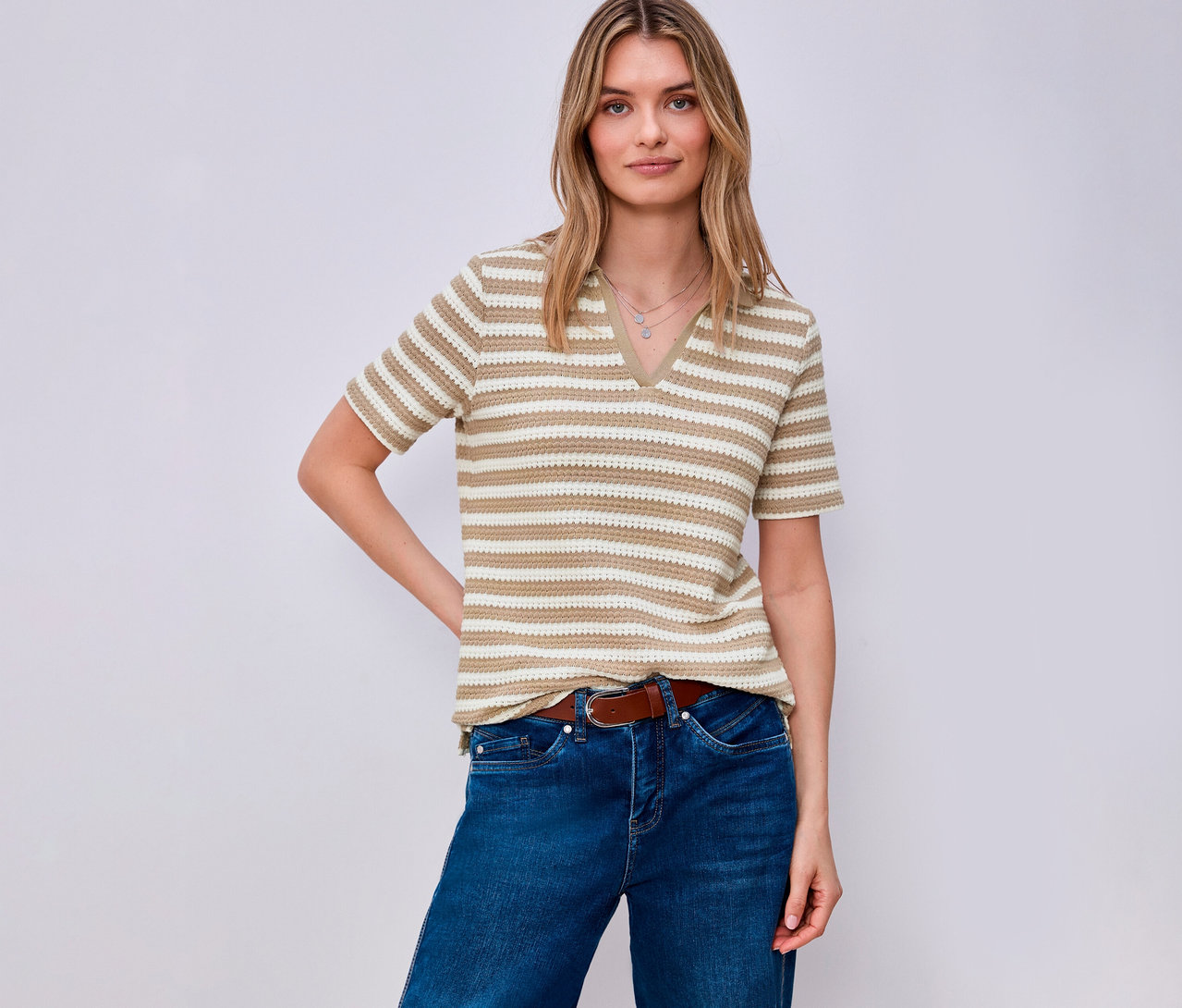 Kobieta w dżinsach i brązowym pasku ma na sobie koszulkę z dzianiny Street One w paski. Pozuje na jasnym tle.