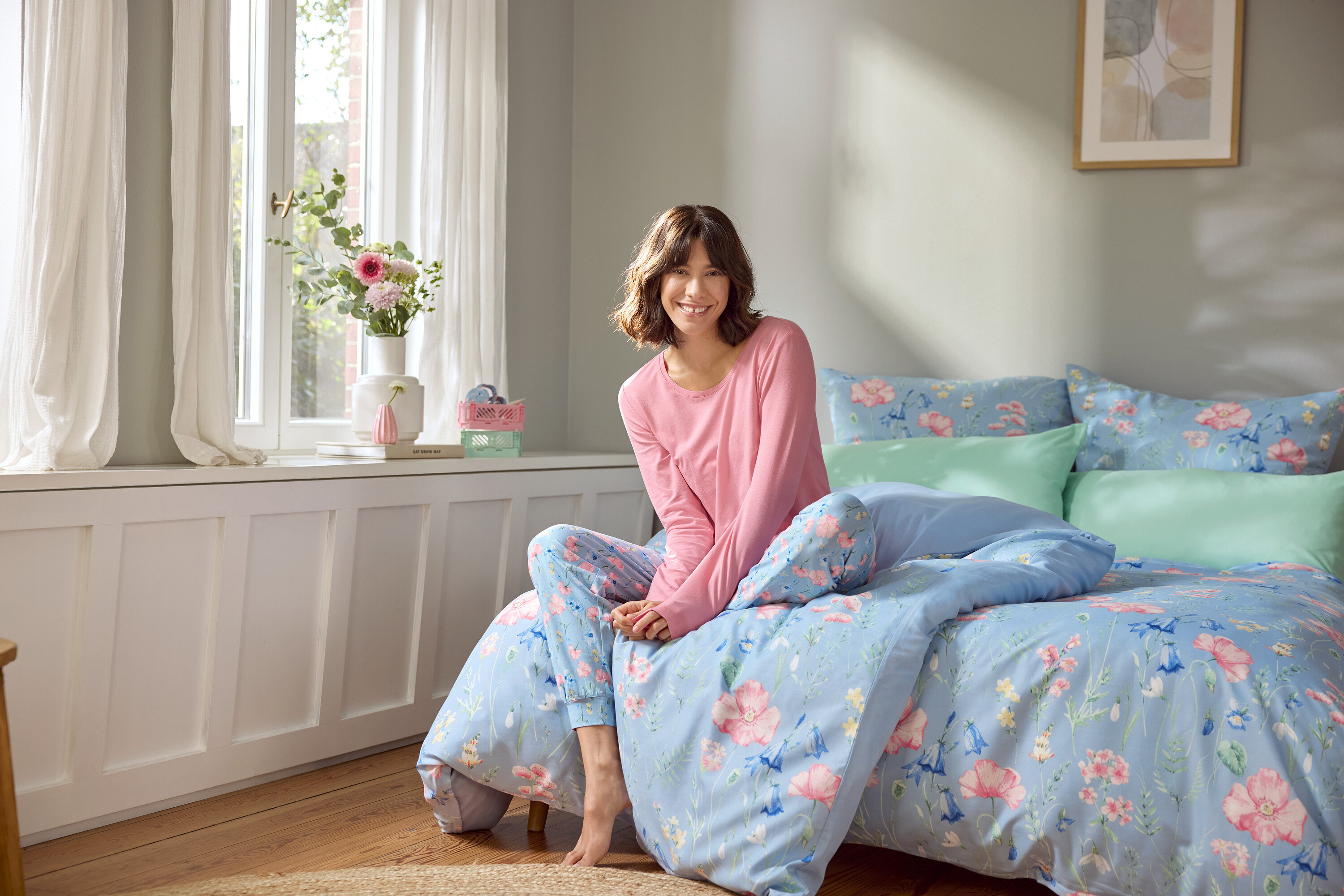 Kobieta siedzi na łóżku z jasnoniebieską pościelą w kwiaty.