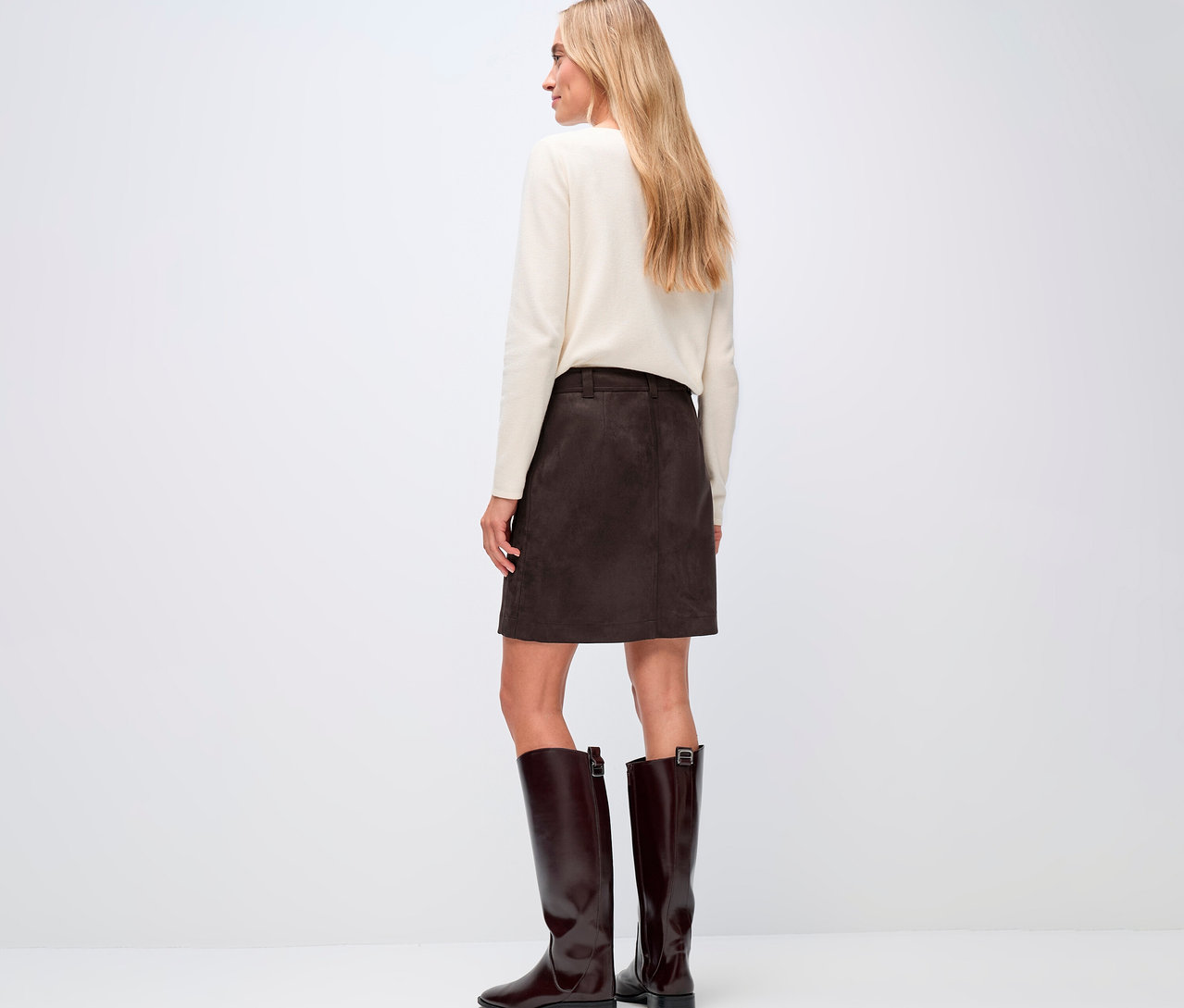 Kobieta widziana od tyłu, ubrana w kremowy sweter i brązową spódnicę welurową od Street One oraz brązowe buty.
