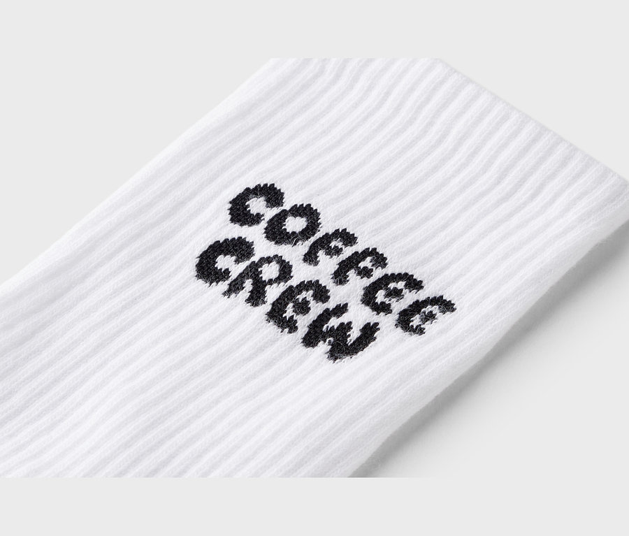 Zbliżenie na białą skarpetę z czarnym napisem "Coffee Crew".