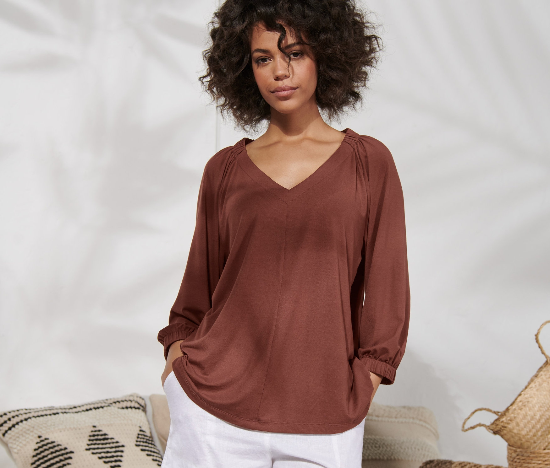 Kobieta pozuje w terakotowej koszulce z marszczeniem i białych szortach.