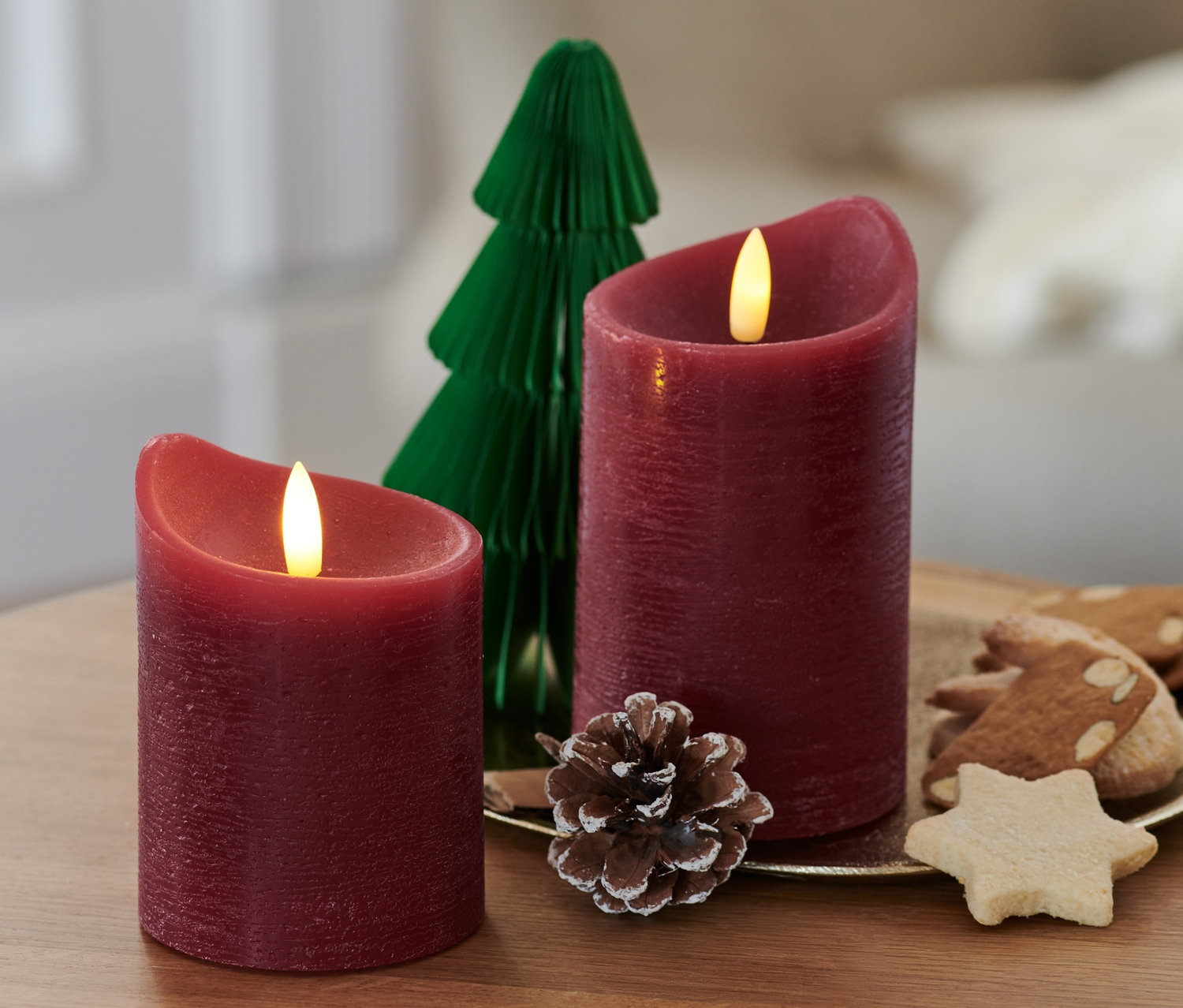 Dwie czerwone świece LED z prawdziwego wosku i zielona papierowa choinka na drewnianym stoliku.