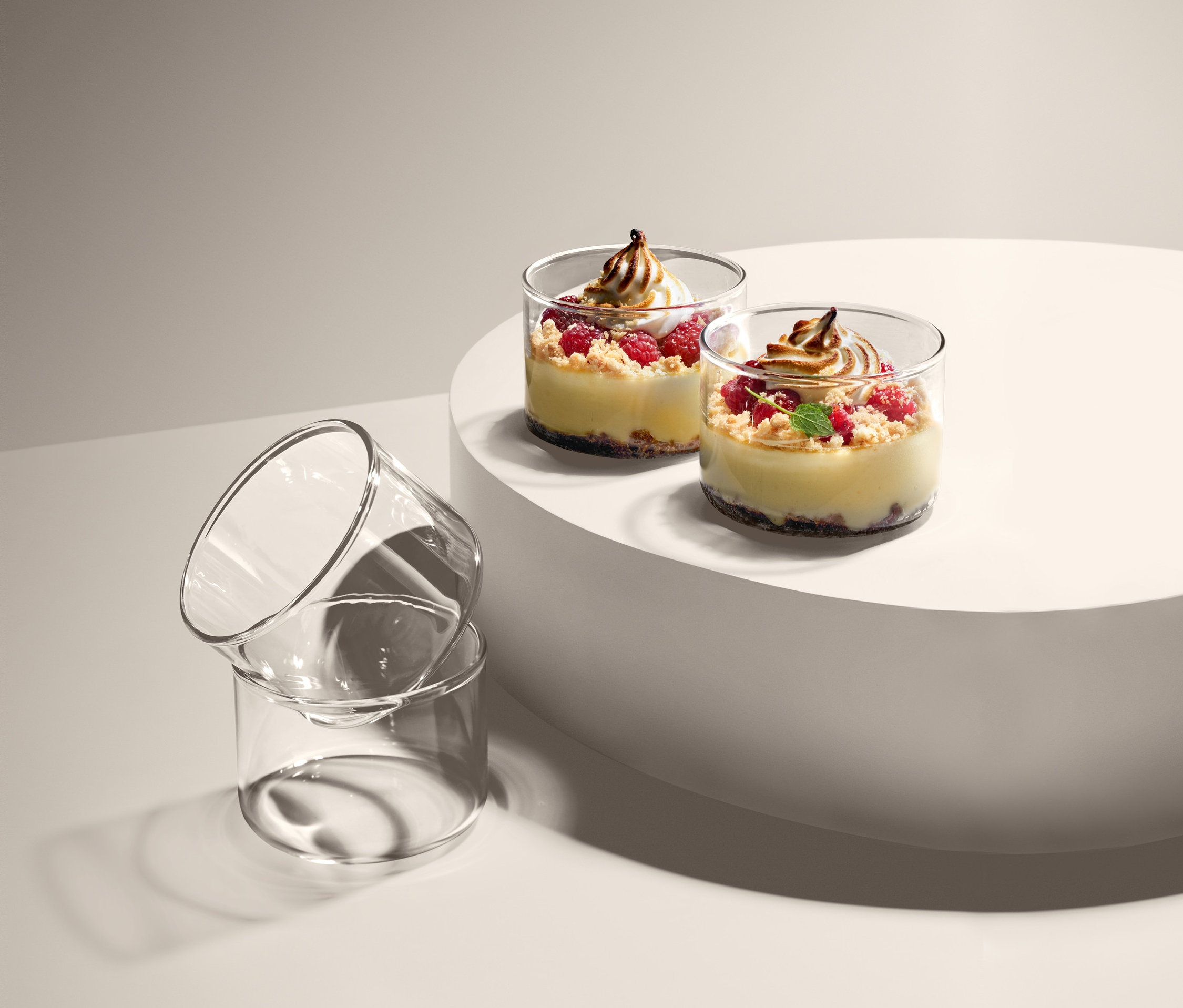 Dwa desery w foremkach do porcjowania i zapiekania, 4 sztuki, na białym postumencie, obok dwa puste foremki do porcjowania i zapiekania, 4 sztuki, ułożone jeden na drugim.