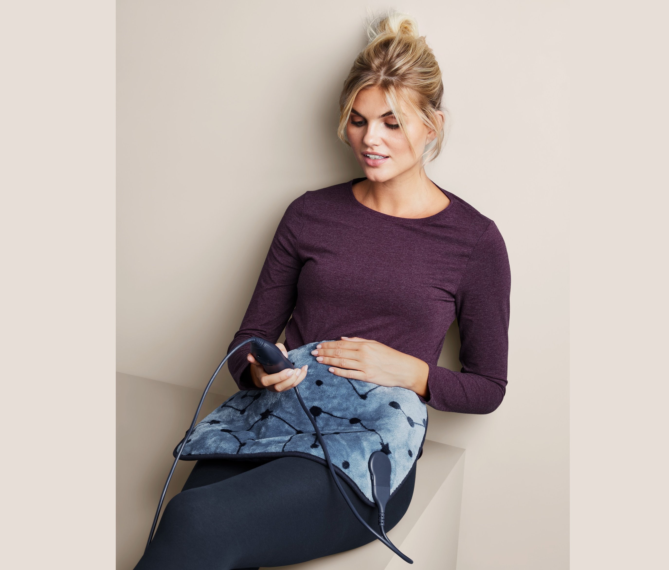 Kobieta siedzi i trzyma małą poduszkę elektryczną.