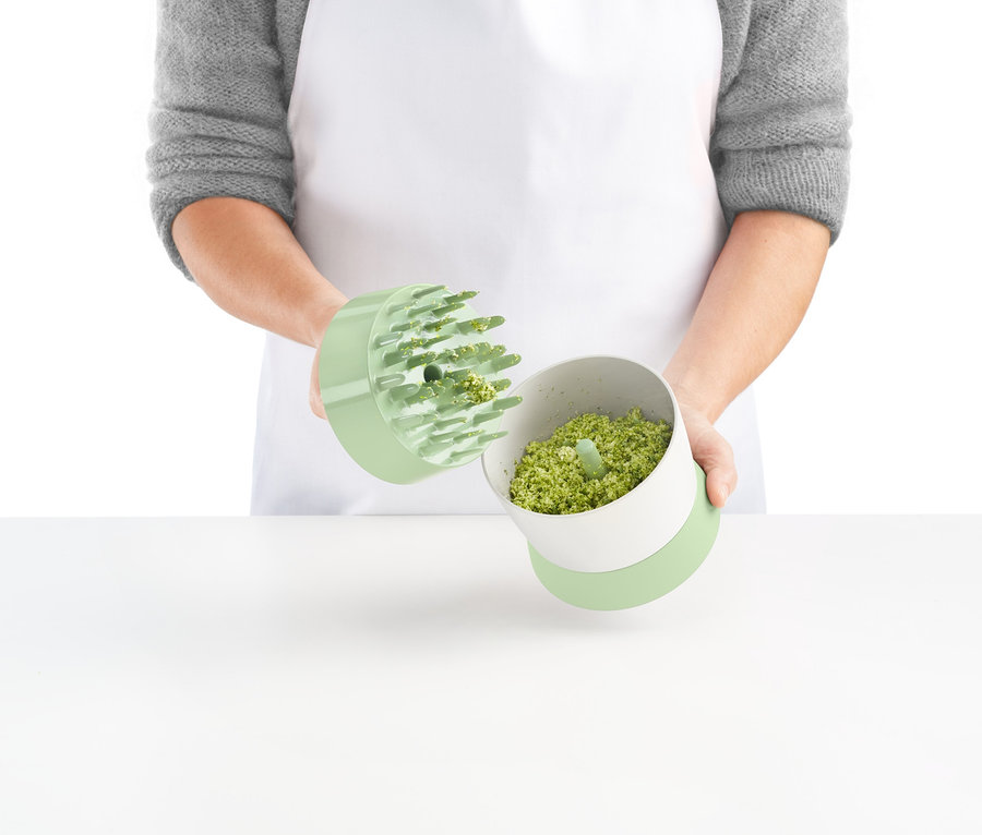 Osoba trzyma rozdrabniacz do warzyw z pokrojonymi warzywami.