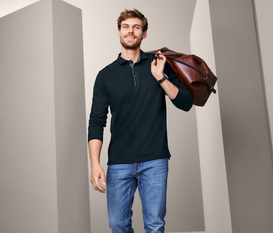 Mężczyzna z brązową torbą na ramieniu i w dżinsowej kurtce ma na sobie granatową męską koszulkę polo z długimi rękawami.