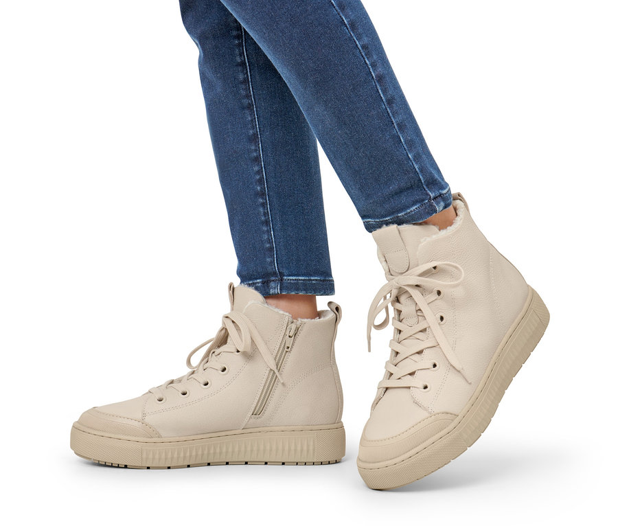 Nogi w jeansach noszą beżowe ocieplane buty typu sneakers ze skóry.